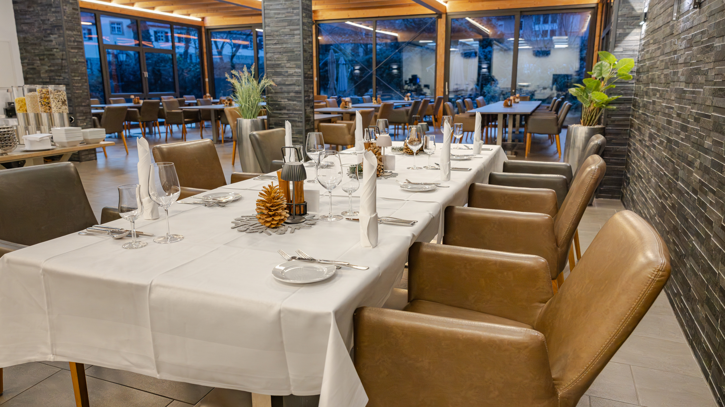 Lange, weiß eingedeckte Tafel mit Kerzen im Wintergarten zur blauen Stunde