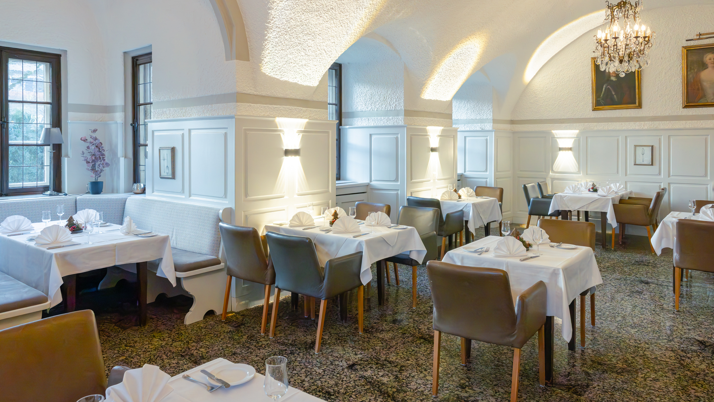 Gewölbesaal des Restaurants mit Kronleuchtern, Ahnenporträts und eingedeckten Tischen
