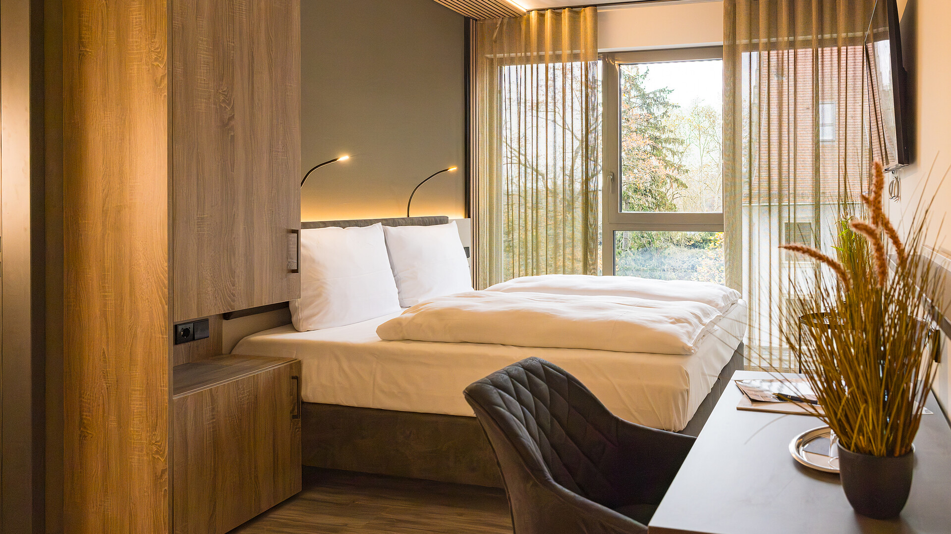 Blick aus einem Neubauzimmer durch die raumhohe Fensterfront in die Baumkronen