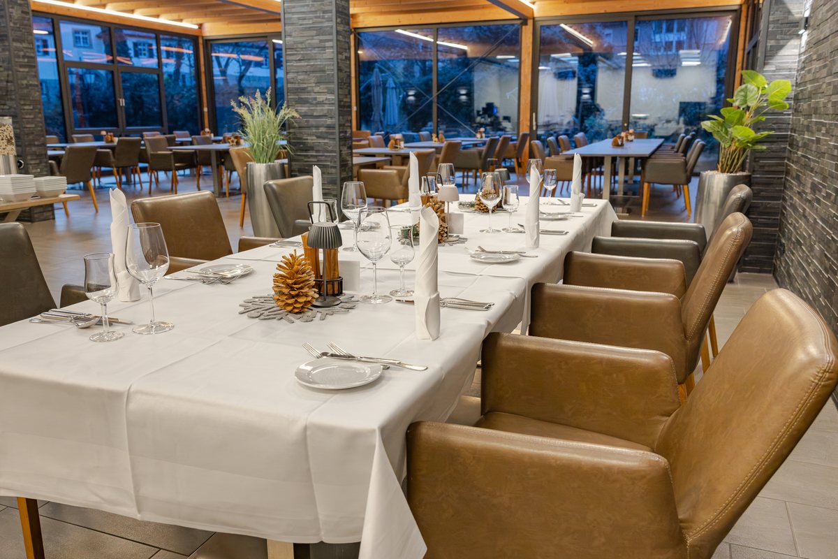 Lange, weiß eingedeckte Tafel mit Kerzen im Wintergarten zur blauen Stunde