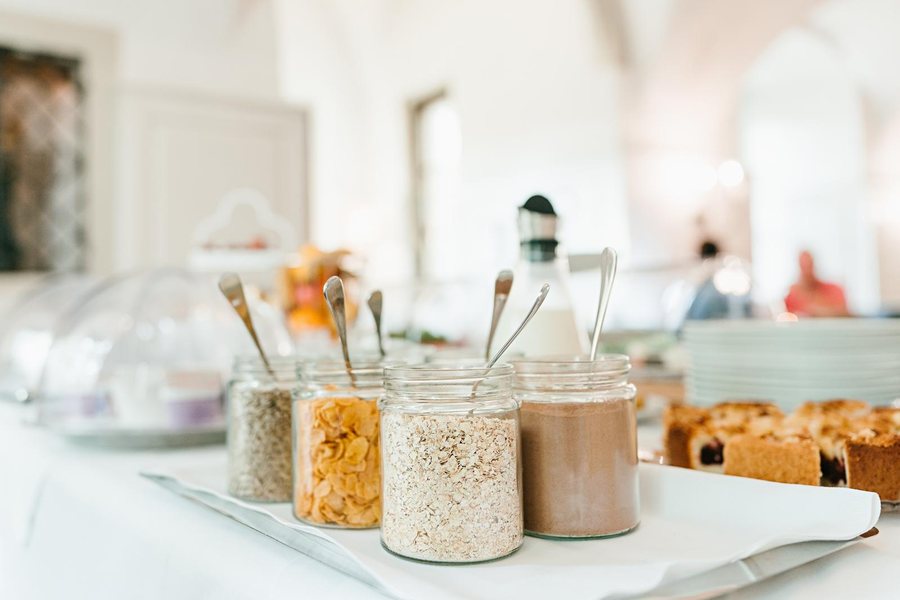 Frühstücksbuffet: Müsli, Cornflakes und Haferflocken in Gläsern, dahinter Kuchen